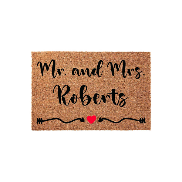 Personalized Mr. and Mrs. wedding doormat made of natural coir fiber, featuring elegant black script text and a decorative arrow design with a small red heart centered on a plain white studio background for a clean entryway look.