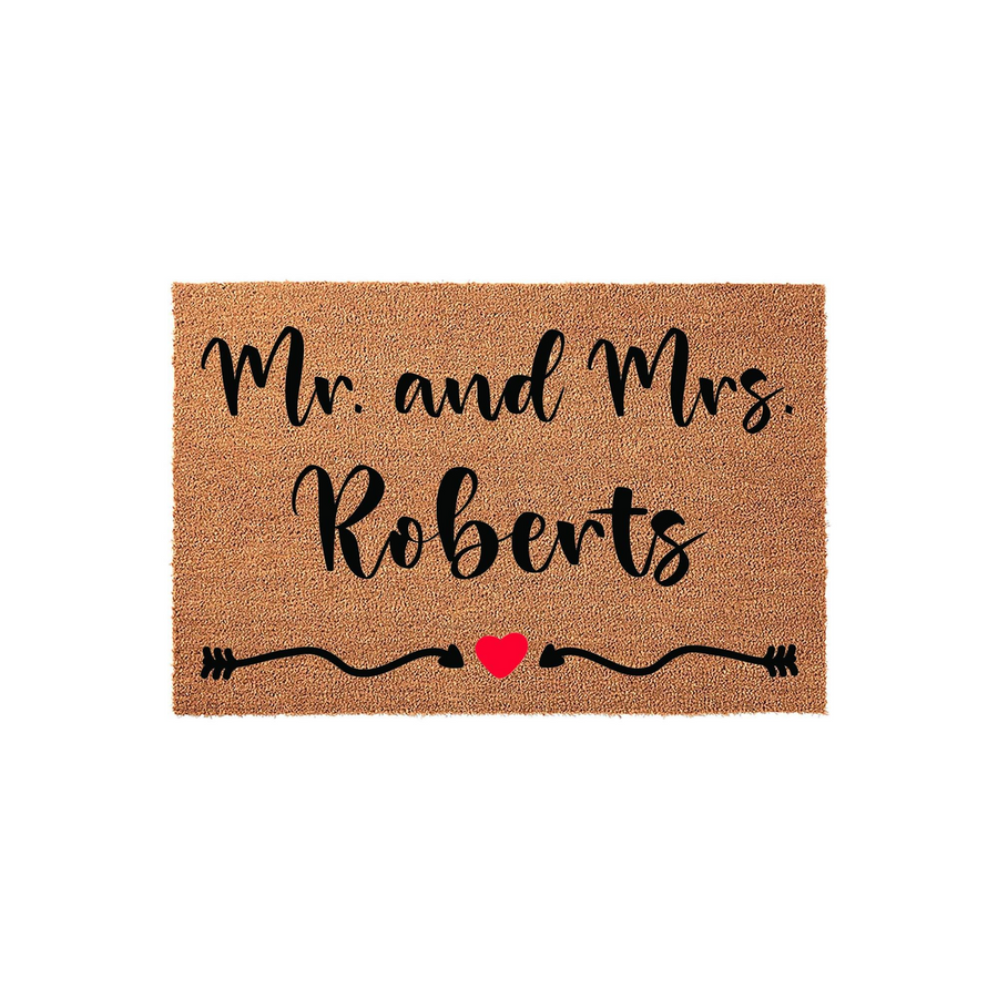Personalized Mr. and Mrs. wedding doormat made of natural coir fiber, featuring elegant black script text and a decorative arrow design with a small red heart centered on a plain white studio background for a clean entryway look.