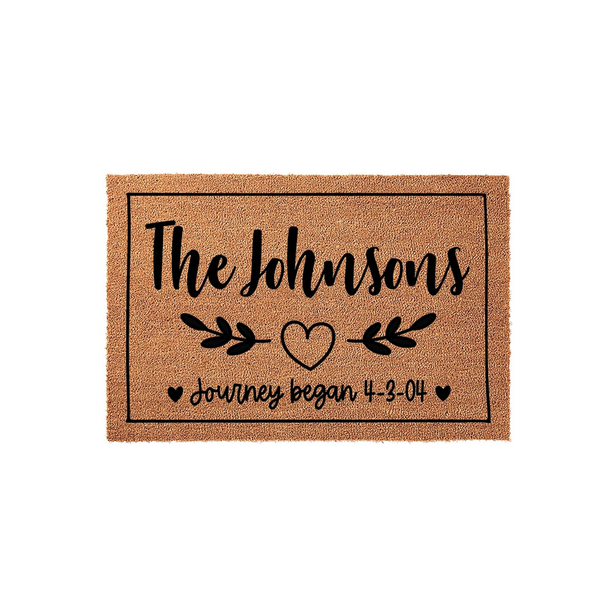 Personalized family name coir doormat featuring a rustic brown texture, black script text, a central heart icon with leafy branches, and the phrase journey began with a custom date to celebrate a wedding or anniversary milestone.