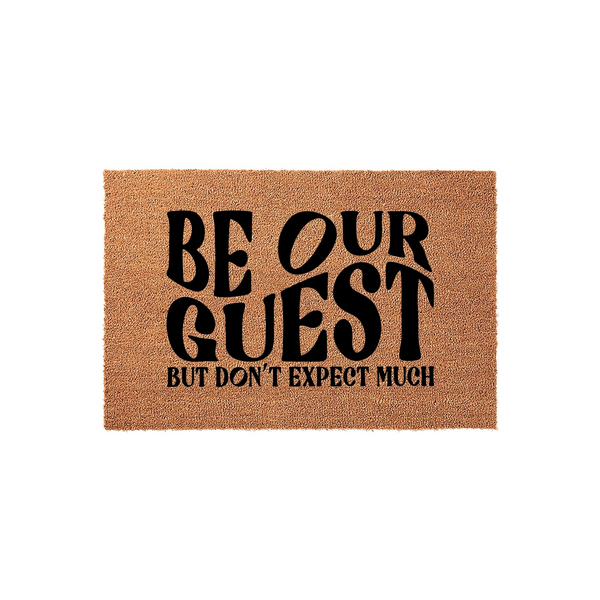Funny Be Our Guest Doormat featuring bold black typography on a natural coir fiber mat, perfect for adding a humorous touch to your front porch decor while welcoming visitors with a witty and sarcastic message about low