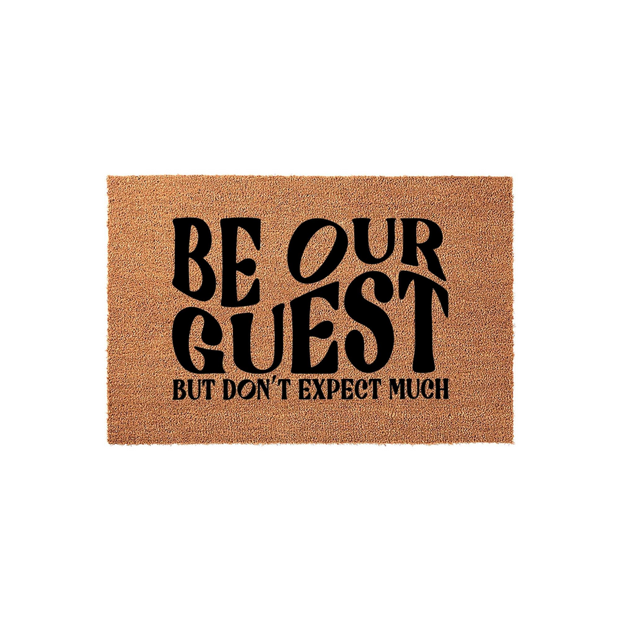 Funny Be Our Guest Doormat featuring bold black typography on a natural coir fiber mat, perfect for adding a humorous touch to your front porch decor while welcoming visitors with a witty and sarcastic message about low