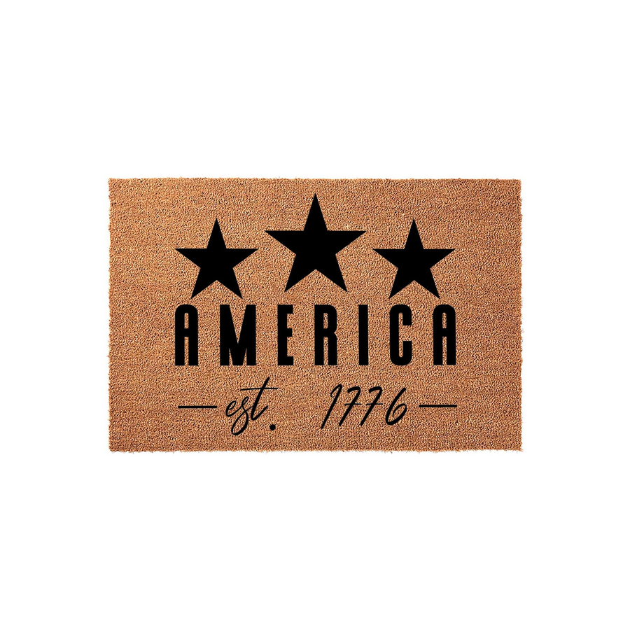 America Est 1776 Coir Doormat featuring three bold black stars above the word AMERICA and the established date in a stylish script font, all set against a natural tan coconut fiber background for a patriotic front porch entryway
