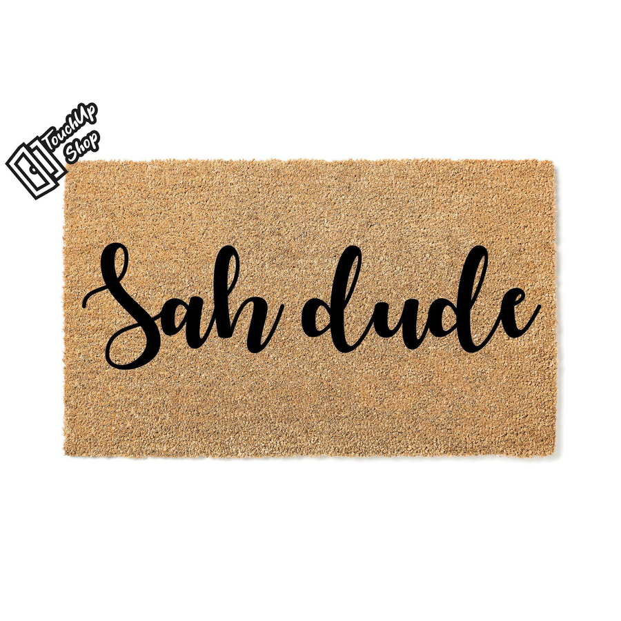 Sah dude coir doormat featuring a natural tan fiber texture and bold black script lettering that says Sah dude, providing a fun and casual welcome for your front porch or entryway decor in a simple studio product shot.