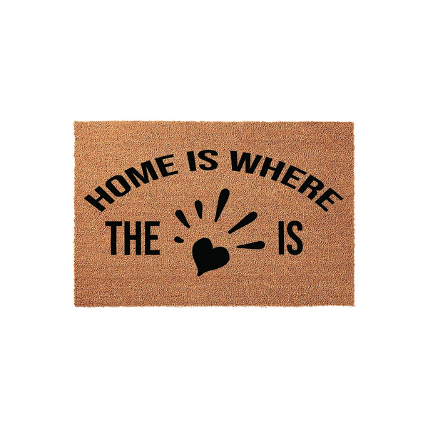 Home Is Where The Heart Is coir doormat featuring a natural tan fiber texture and bold black lettering with a central heart icon, creating a welcoming entrance decor piece for any front porch or entryway floor.