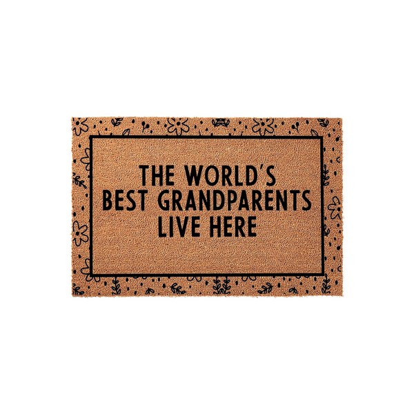 The World's Best Grandparents Live Here coir doormat features a natural tan fiber texture with a black border decorated in a whimsical floral pattern, making it a charming entryway accent for a home shared by beloved grandparents.
