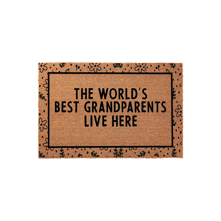 The World's Best Grandparents Live Here coir doormat features a natural tan fiber texture with a black border decorated in a whimsical floral pattern, making it a charming entryway accent for a home shared by beloved grandparents.