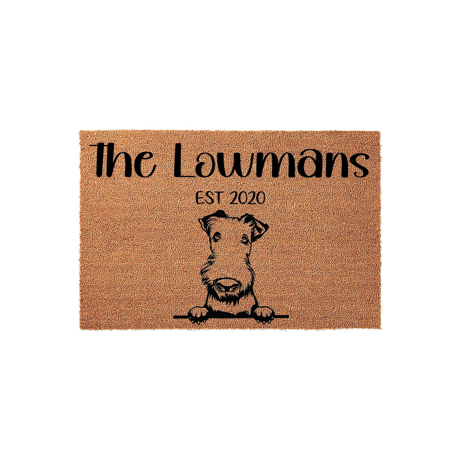 Personalized Airedale Terrier doormat featuring a custom family name and established year printed in black ink on a natural coir fiber mat, showcasing a cute dog illustration peeking over a horizontal line for a welcoming home