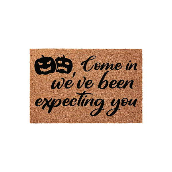 Halloween coir doormat featuring two black jack-o-lantern pumpkin icons and the text Come in we have been expecting you printed in a bold script font on a natural tan fiber background, perfect for seasonal fall porch decor.