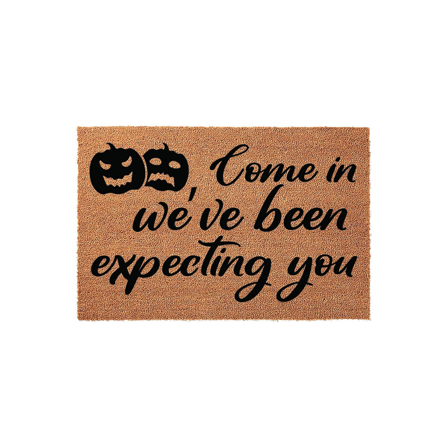 Halloween coir doormat featuring two black jack-o-lantern pumpkin icons and the text Come in we have been expecting you printed in a bold script font on a natural tan fiber background, perfect for seasonal fall porch decor.