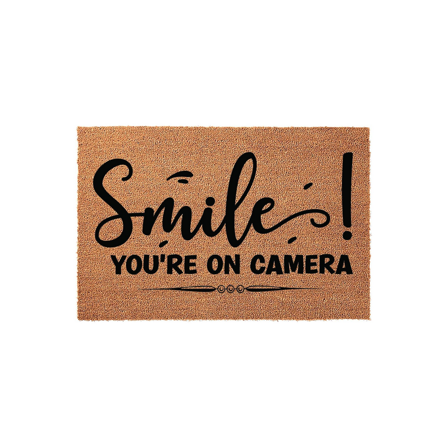 Smile You're On Camera coir doormat featuring a natural brown fiber texture with bold black text that reads Smile You're On Camera, making it a humorous and functional front porch decor piece for any home entrance or