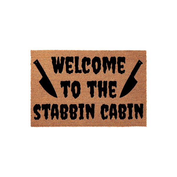 Horror themed Welcome to the Stabbin Cabin doormat featuring a natural coir fiber texture with bold black text and two large kitchen knife silhouettes flanking the word welcome on a plain white background.
