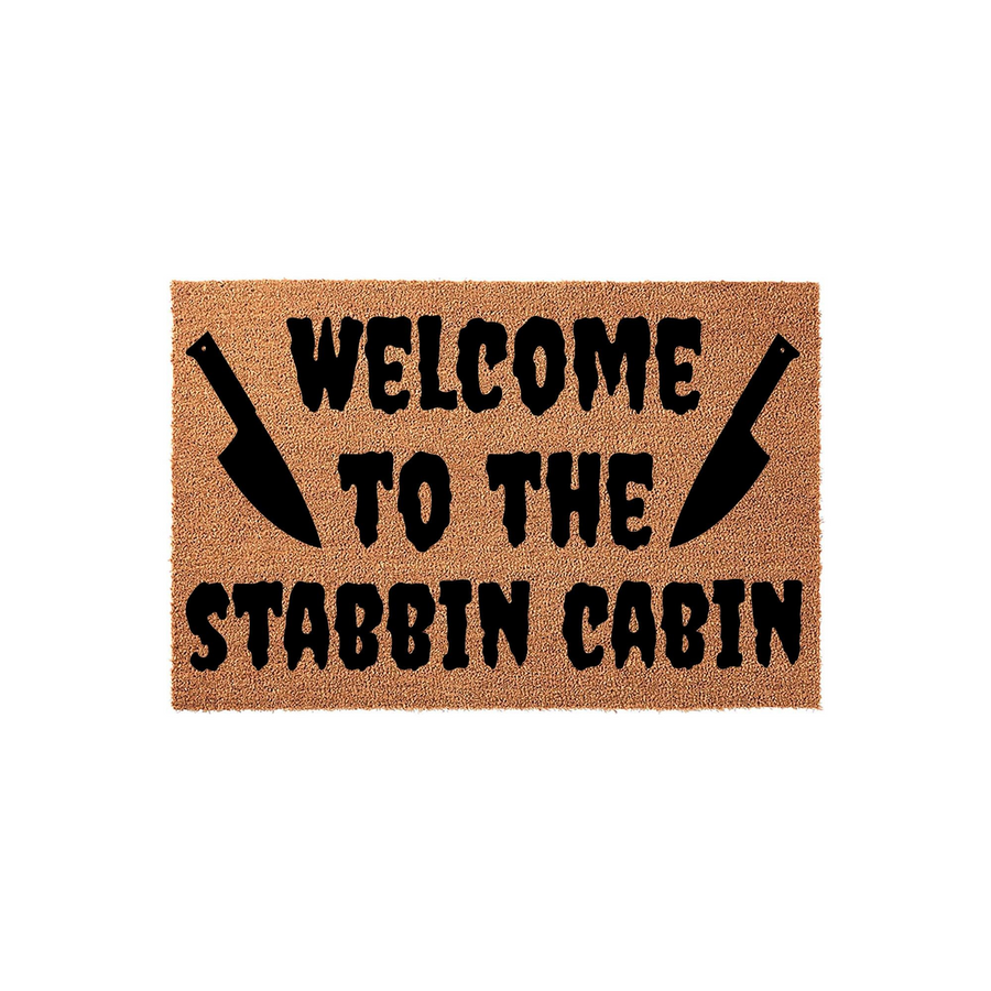 Horror themed Welcome to the Stabbin Cabin doormat featuring a natural coir fiber texture with bold black text and two large kitchen knife silhouettes flanking the word welcome on a plain white background.