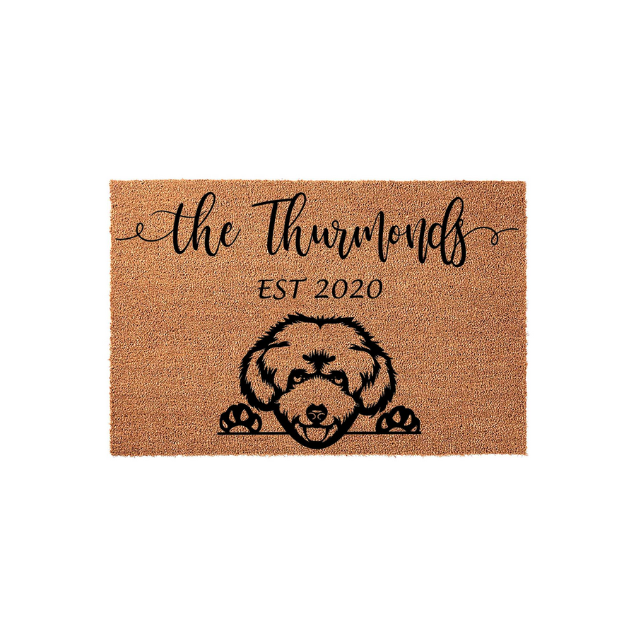 Personalized Doodle Dog Coir Doormat featuring a cute illustrated dog peeking over the bottom edge, customized with a family name and established year printed in black ink on a natural tan textured fiber background for a home