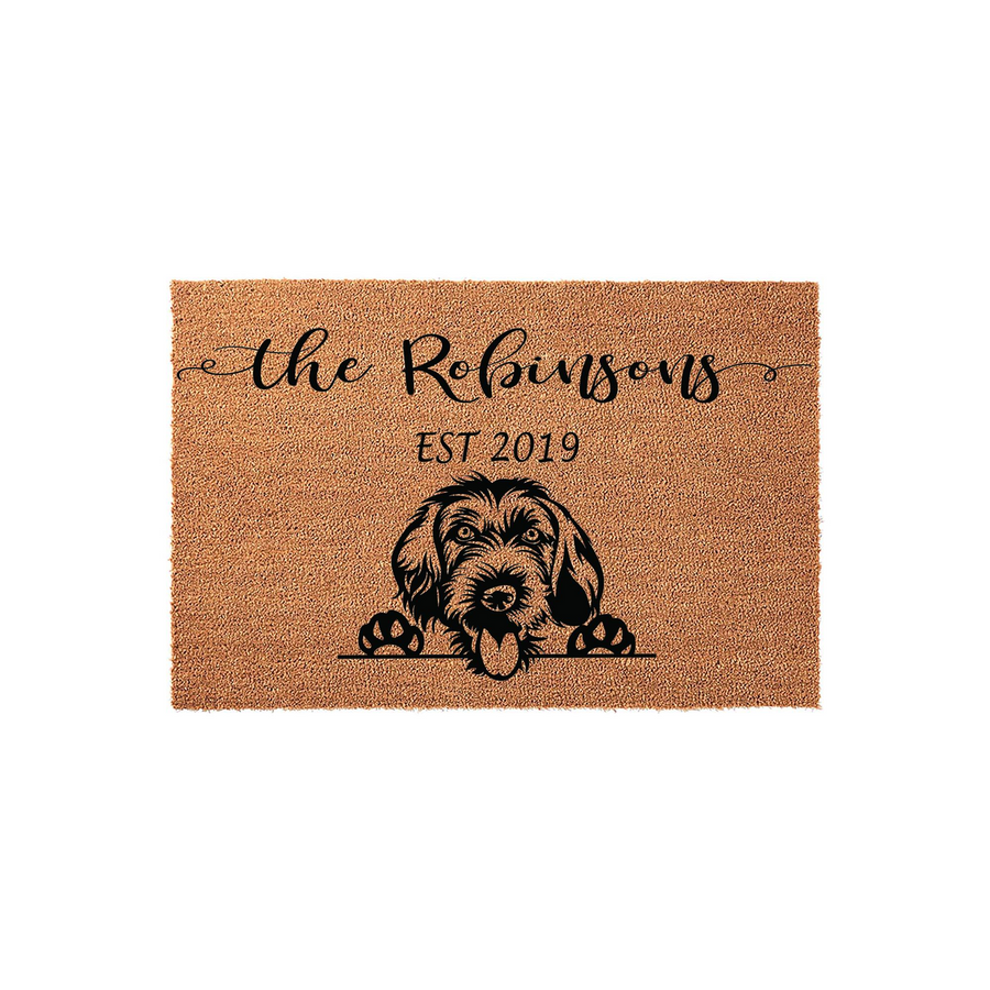Personalized Doodle dog doormat featuring a cute shaggy dog illustration peeking over a line, customized with a family name and established year on a natural coir fiber mat that adds a welcoming touch to any front porch entryway.