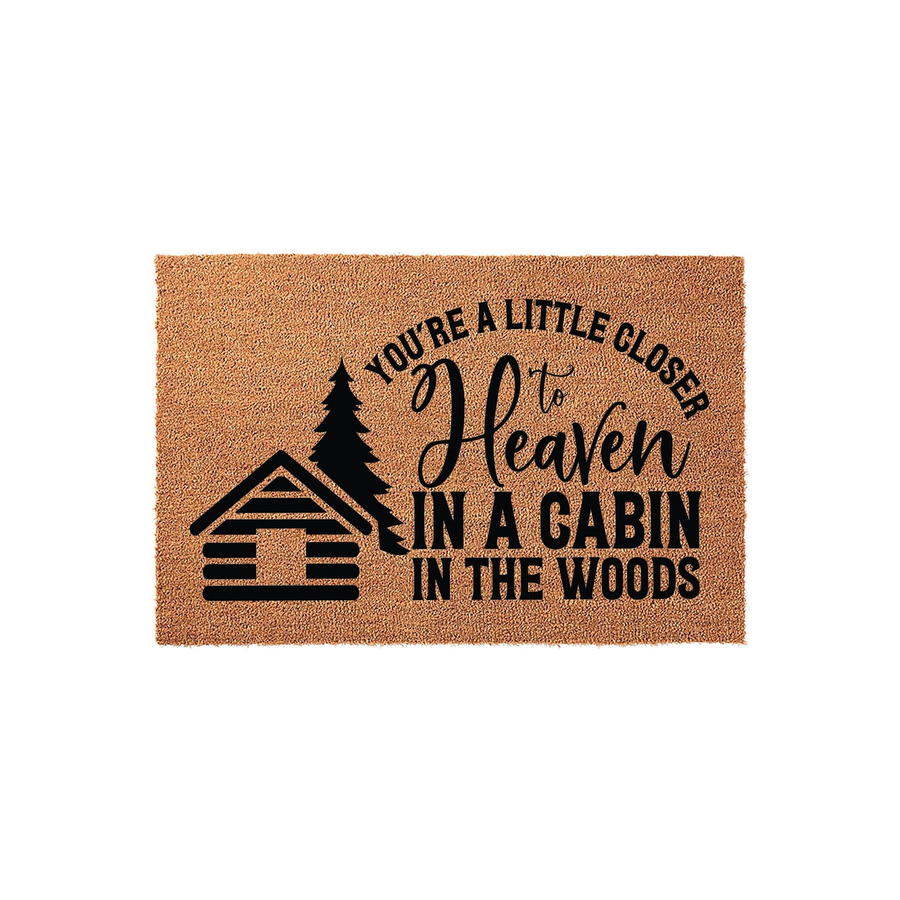 Cabin in the Woods Doormat featuring a rustic log cabin and pine tree graphic with the text You are a little closer to heaven in a cabin in the woods, printed in black ink on a natural tan coir fiber mat against a plain white