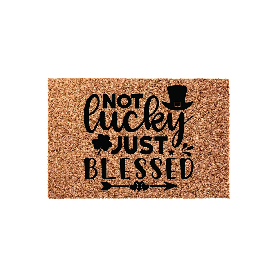 St. Patrick's Day coir doormat featuring the text Not Lucky Just Blessed in black ink, decorated with a leprechaun top hat, a shamrock, and a decorative arrow design on a natural brown fiber background for a festive front porch