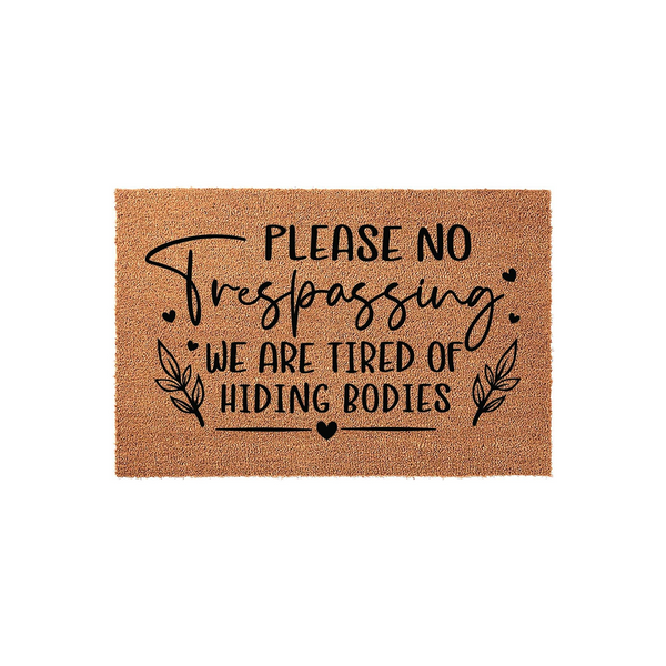 Funny No Trespassing Doormat featuring a natural coir texture with black text that reads Please No Trespassing We Are Tired Of Hiding Bodies, accented by decorative leaf sprigs and small hearts on a simple white studio background.