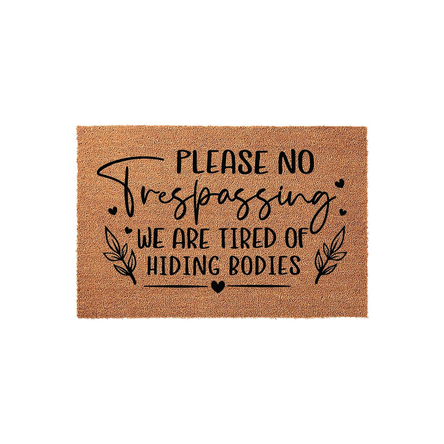 Funny No Trespassing Doormat featuring a natural coir texture with black text that reads Please No Trespassing We Are Tired Of Hiding Bodies, accented by decorative leaf sprigs and small hearts on a simple white studio background.