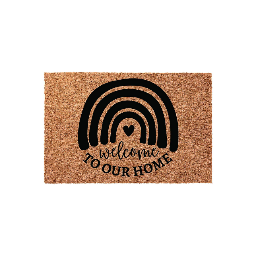 Boho Rainbow Welcome Doormat featuring a natural coir texture and a bold black graphic of a rainbow with a small heart, displaying the text Welcome To Our Home in a stylish script and serif font combination on a plain white