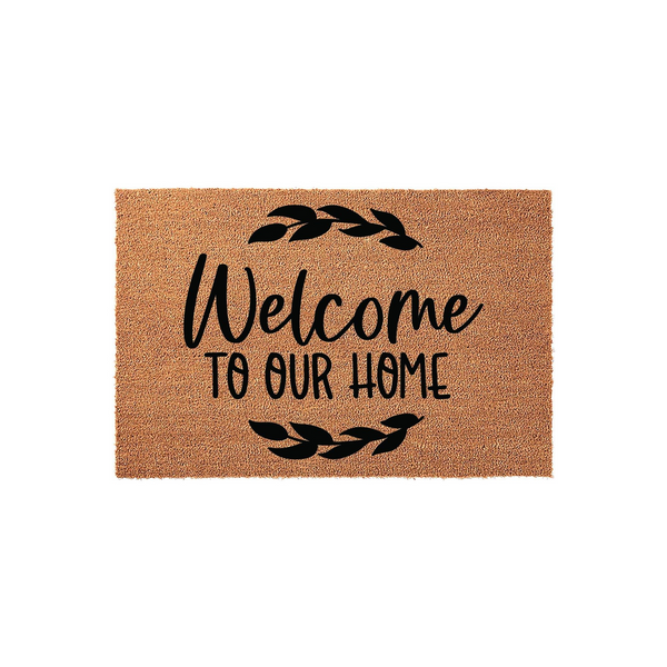 Welcome To Our Home coir doormat featuring a natural tan fiber texture and black printed text with decorative leaf accents, providing a rustic and inviting entryway decor piece for your front porch or house entrance.