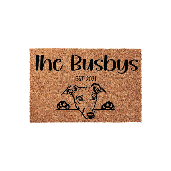 Personalized Greyhound Dog Doormat featuring a cute illustration of a dog peeking over the edge, with custom family name text and an established year printed in black on a natural brown coir fiber welcome mat for your front porch.