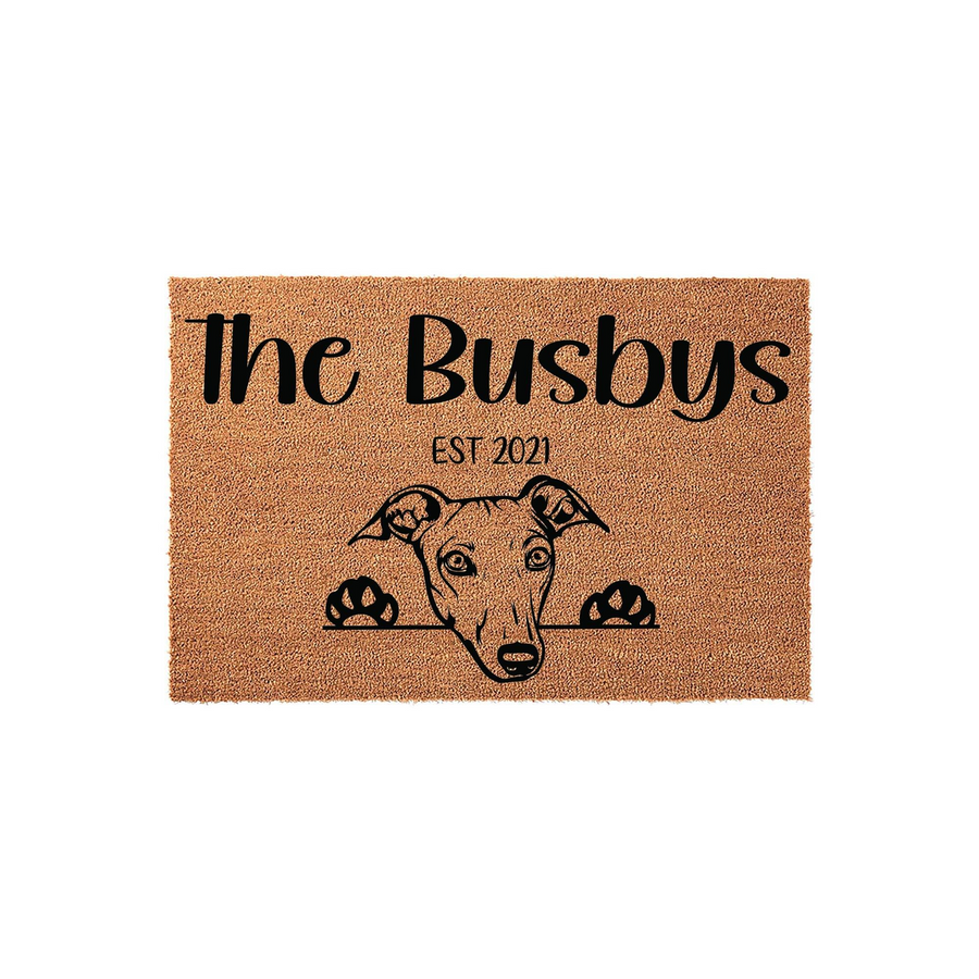 Personalized Greyhound Dog Doormat featuring a cute illustration of a dog peeking over the edge, with custom family name text and an established year printed in black on a natural brown coir fiber welcome mat for your front porch.