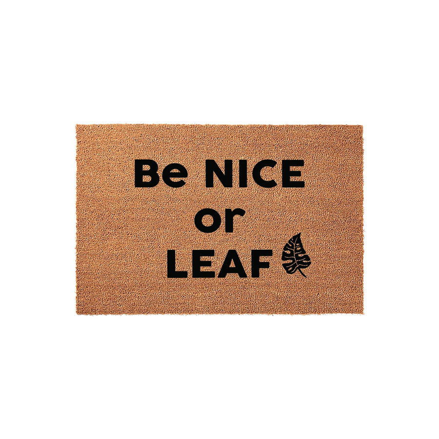 Be Nice or Leaf funny coir doormat featuring bold black text and a tropical monstera leaf graphic on a natural tan fiber background, creating a humorous and welcoming entrance decor piece for any home porch or front door entryway.