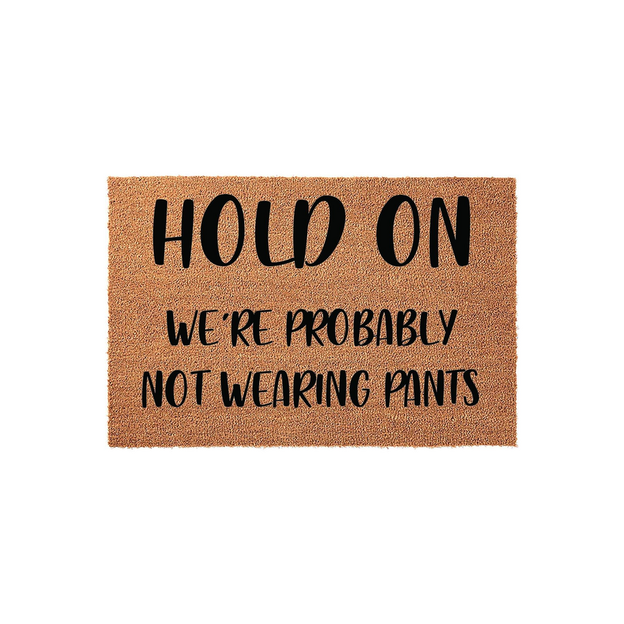 Funny Hold On We Are Probably Not Wearing Pants coir doormat featuring bold black text on a natural brown fiber background, designed as a humorous welcome mat for a front porch or entryway to greet guests with a playful and
