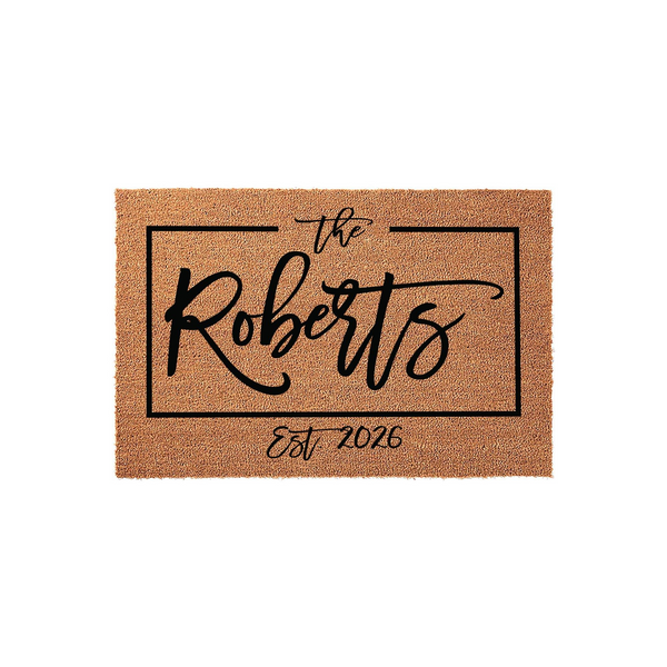 Personalized family name coir doormat featuring a rectangular black border with elegant script text that includes the family name and established year, set against a natural tan textured coconut fiber background for a front porch.