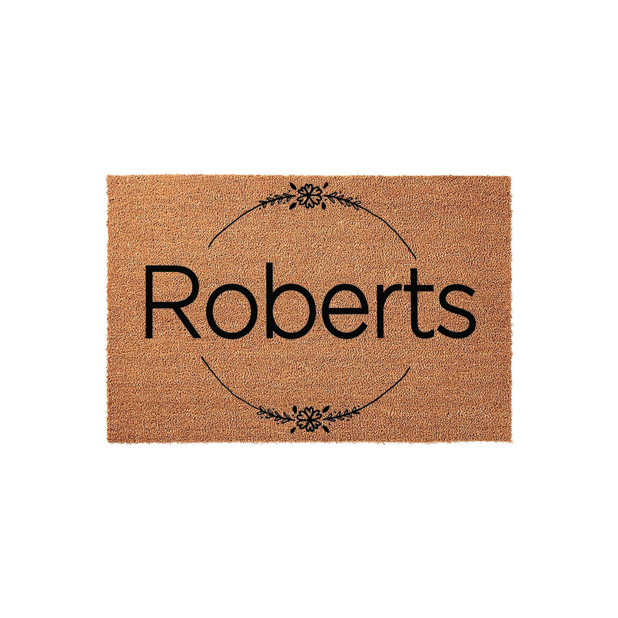 Personalized family name coir doormat featuring a minimalist black floral wreath design surrounding a custom last name, set against a clean white background to showcase the natural textured fibers of this durable outdoor entryway