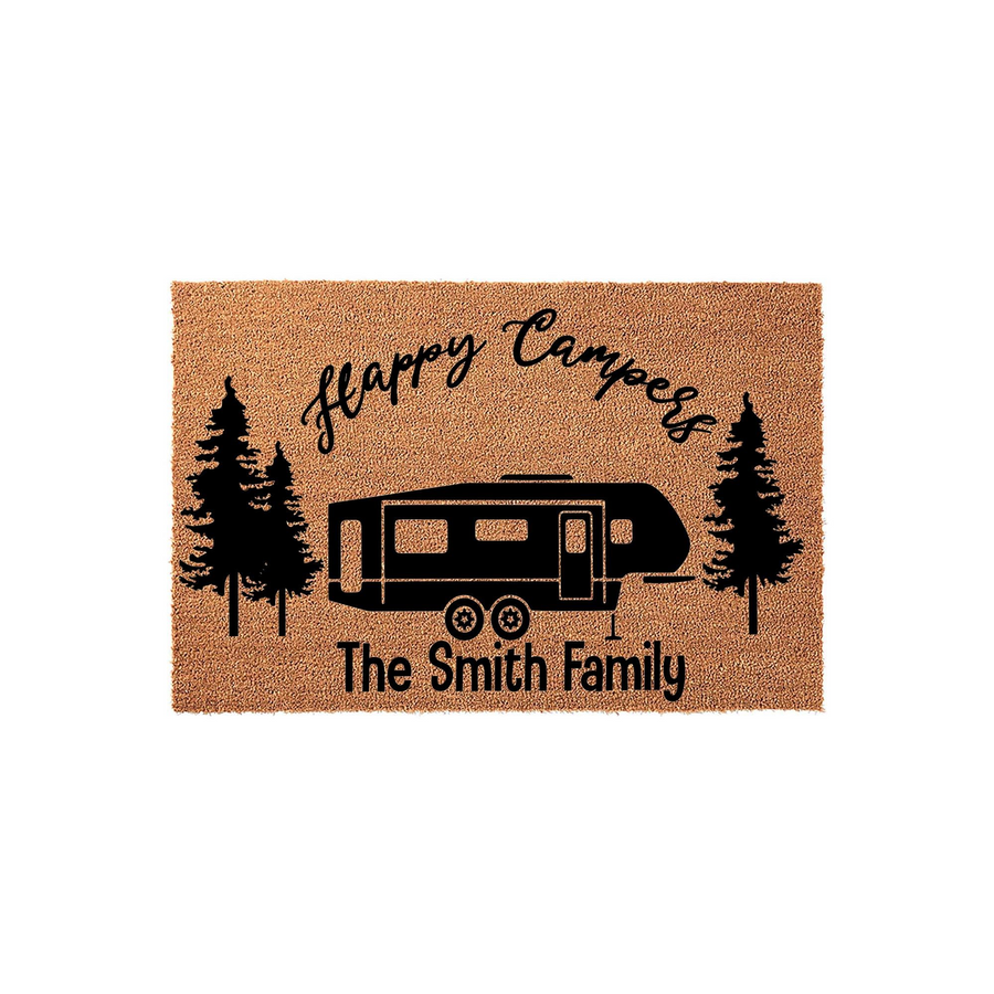 Personalized Happy Campers doormat featuring a black camper trailer graphic flanked by pine trees on a natural coir background, with space for a custom family name printed in a clean, modern font for your outdoor camping decor.