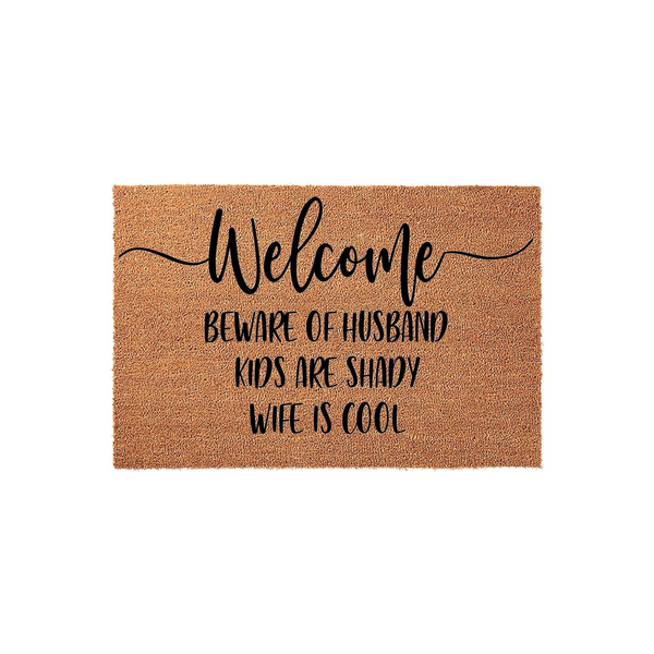 Funny Welcome Doormat featuring natural coir fibers and black text that reads Beware of Husband, Kids Are Shady, Wife Is Cool, making this a humorous and durable outdoor floor mat for a front porch or entryway with a rustic
