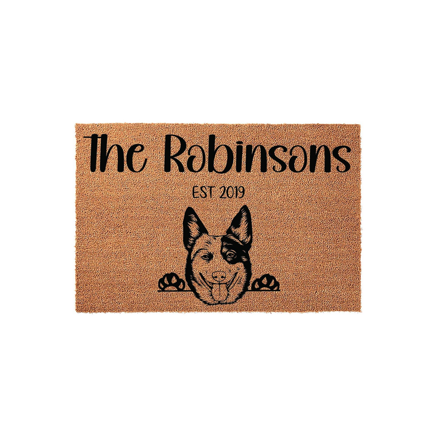Personalized Cattle Dog coir doormat featuring a custom family name and established year, showcasing a cute illustrated Australian Cattle Dog peeking over the bottom edge on a natural tan textured fiber background for a welcoming