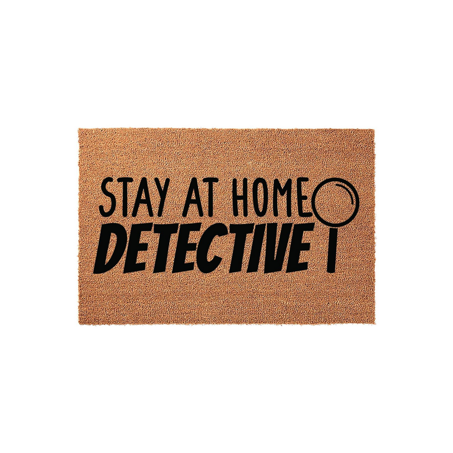 Stay at Home Detective coir doormat featuring bold black text and a magnifying glass icon printed on a natural brown fiber mat, creating a fun and welcoming entryway accessory for true crime fans and mystery lovers.