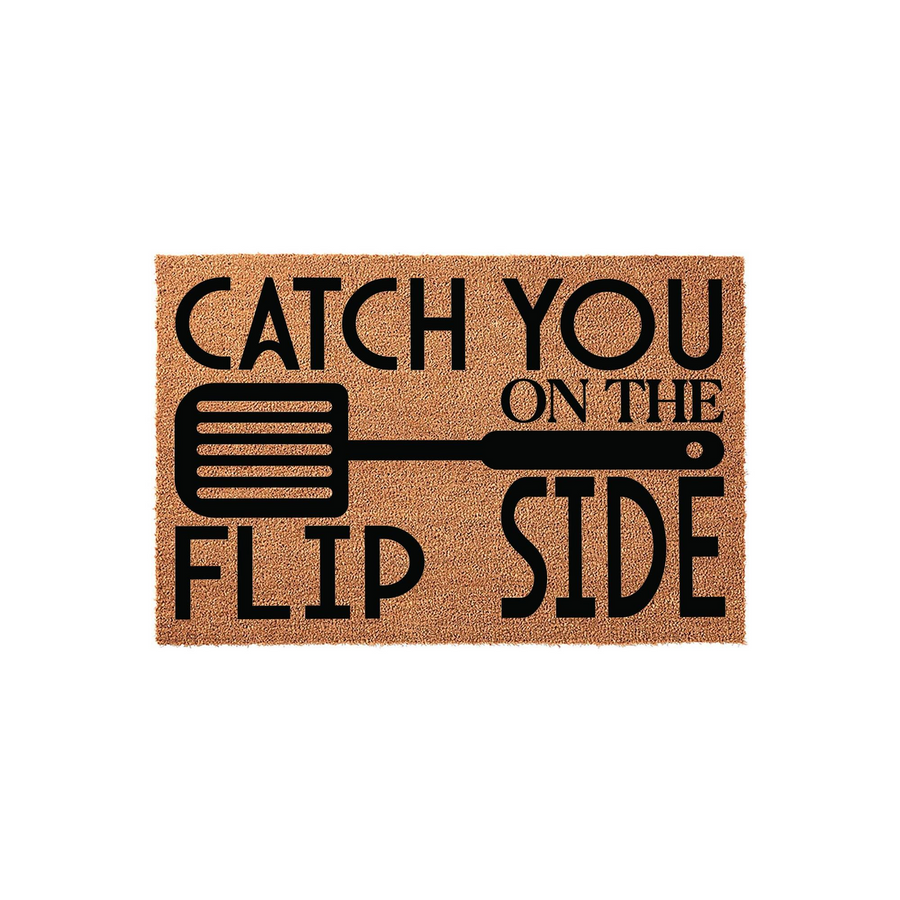 Catch You On The Flip Side funny kitchen doormat made of natural coir fiber, featuring a bold black graphic of a spatula and playful typography centered on a rectangular brown mat against a clean white background for a modern