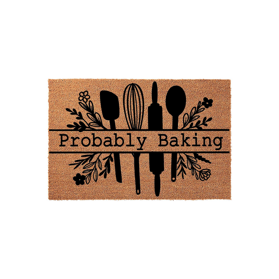 Probably Baking kitchen doormat made of natural coir fiber, featuring a black printed design of a whisk, rolling pin, and spatula surrounded by floral accents on a plain white background for a rustic home decor look.