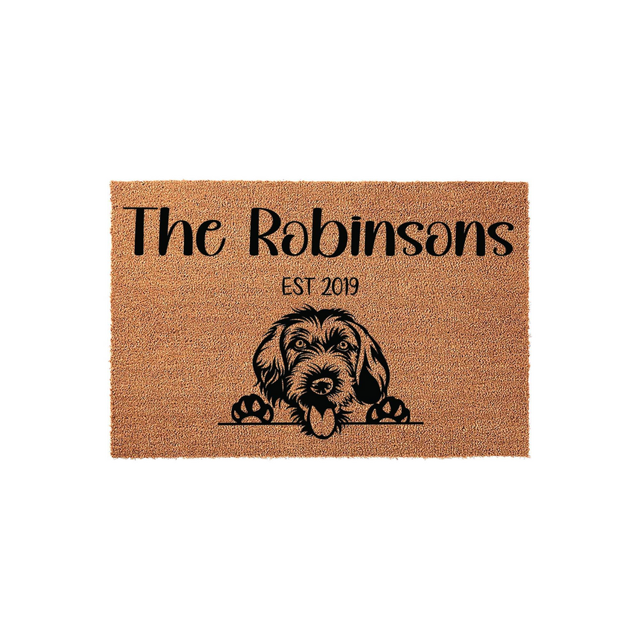 Personalized Doodle Dog Coir Doormat featuring a cute shaggy dog illustration, custom family name text, and an established year date, all printed in black ink on a natural brown textured fiber mat against a clean white background.