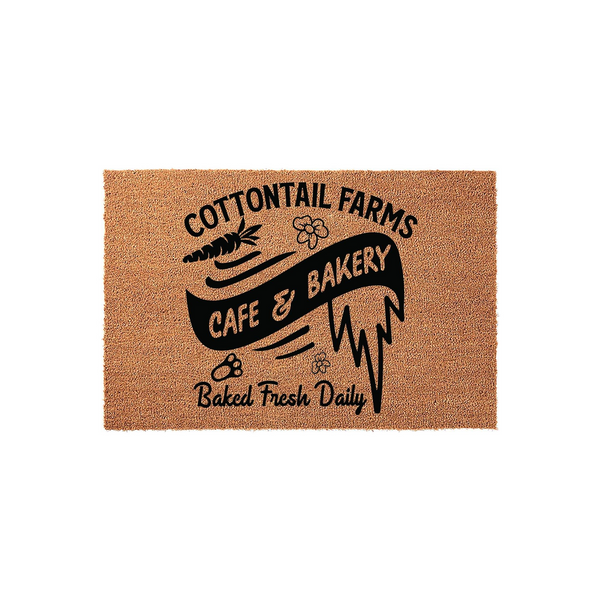 Cottontail Farms Cafe and Bakery coir doormat featuring a rustic brown natural fiber texture with black printed text, a carrot icon, and small flower accents that create a charming farmhouse aesthetic for your front porch