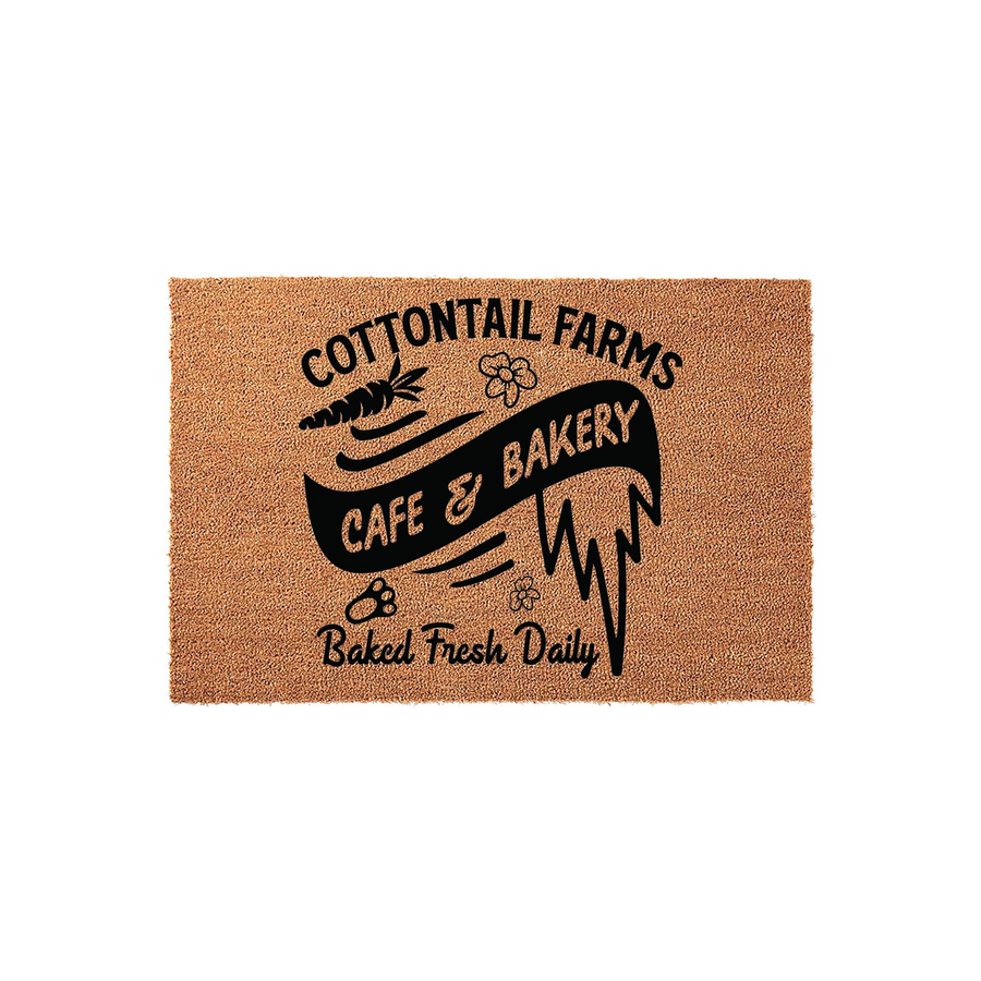 Cottontail Farms Cafe and Bakery coir doormat featuring a rustic brown natural fiber texture with black printed text, a carrot icon, and small flower accents that create a charming farmhouse aesthetic for your front porch