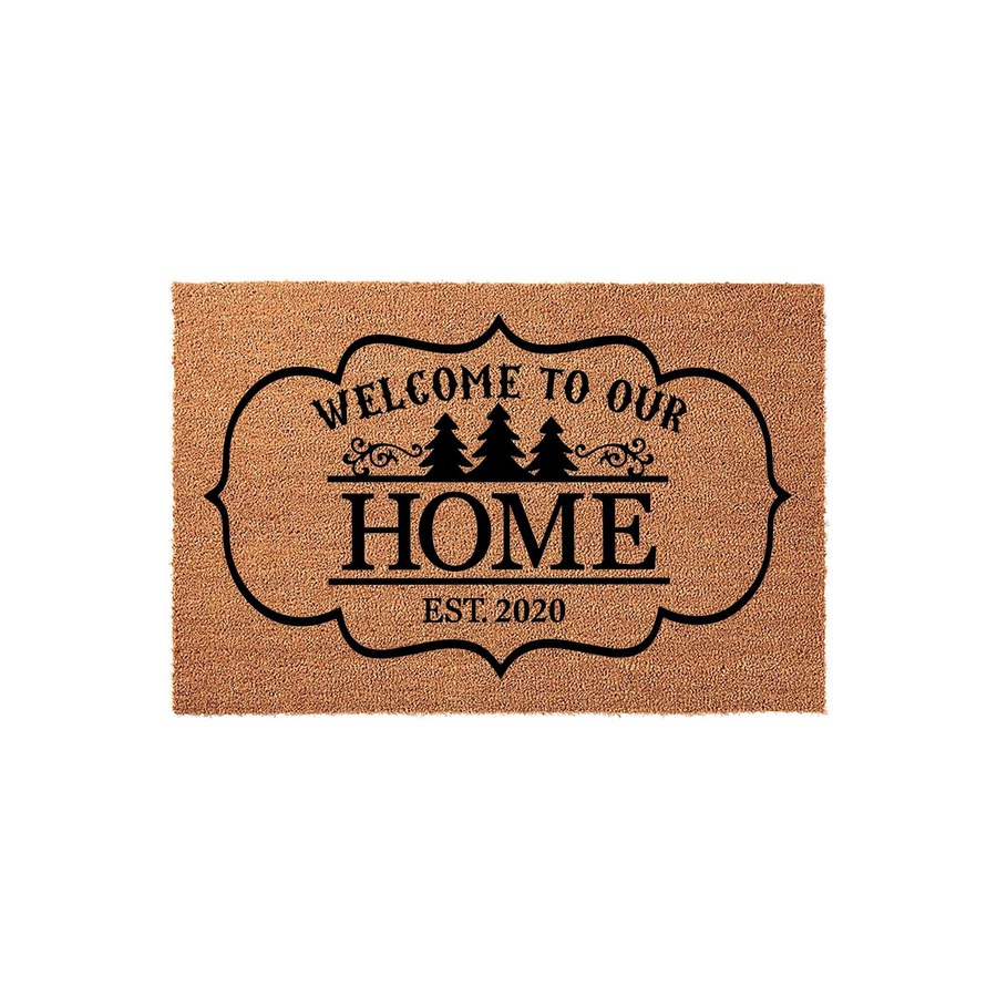 Personalized Welcome To Our Home doormat featuring a rustic coir texture and a black decorative frame with pine tree silhouettes, perfect for a front porch entrance to celebrate a new house or family establishment date of 2020.