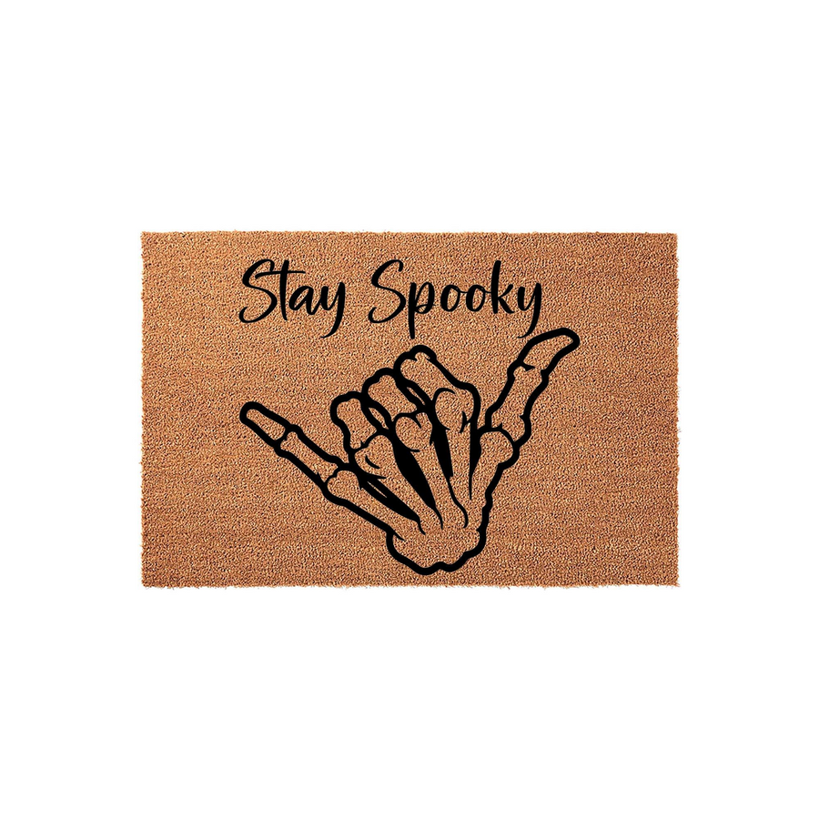 Stay Spooky skeleton hand doormat featuring a natural coir texture and a black shaka hand gesture graphic, providing a fun and festive Halloween entryway decor piece for your front porch or home entrance during the fall season.