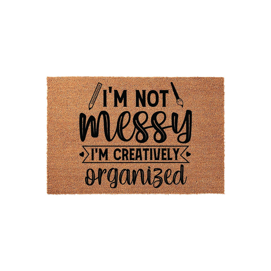 Creatively Organized Coir Doormat featuring a humorous quote about being messy, printed in bold black lettering on a natural brown coconut fiber mat with icons of a pencil and a paintbrush on a clean white studio background.