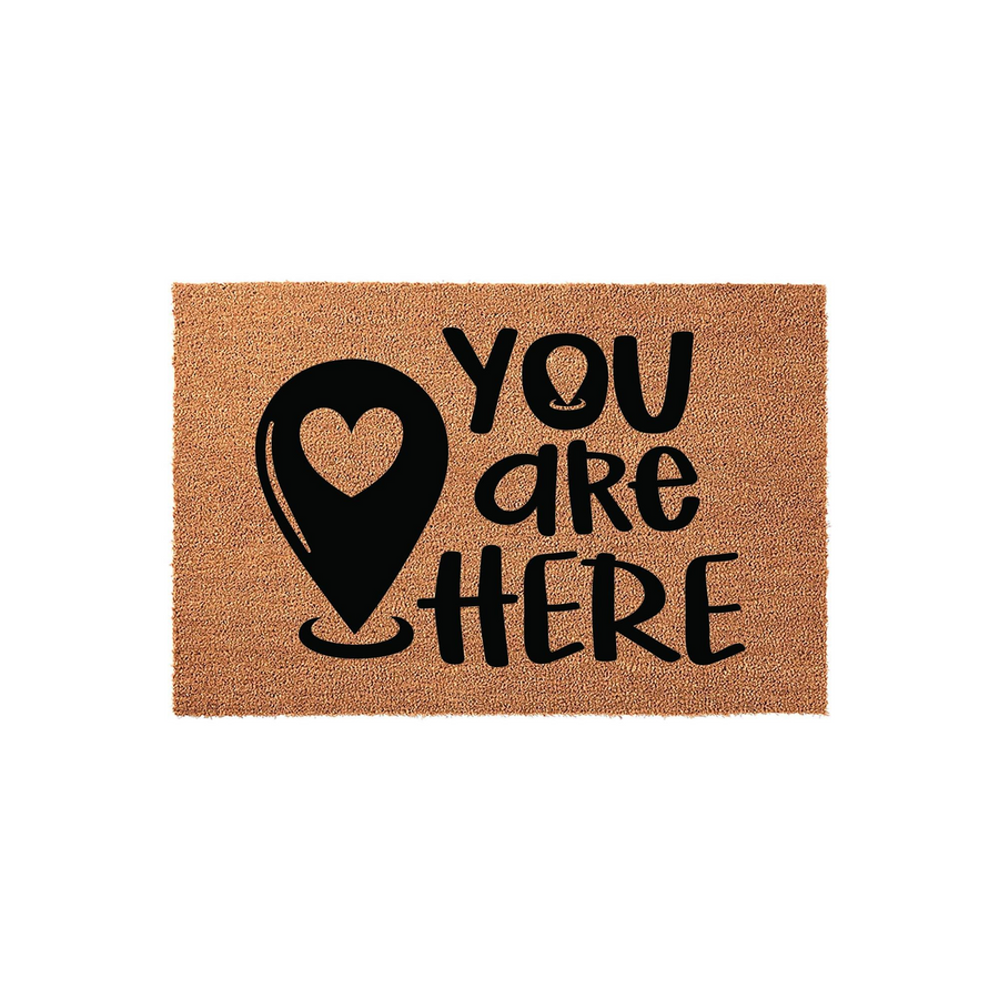 You Are Here Coir Doormat featuring a black map location pin icon with a heart cutout, set against a natural brown textured fiber background to welcome guests to your home with a fun and modern entryway decor style.