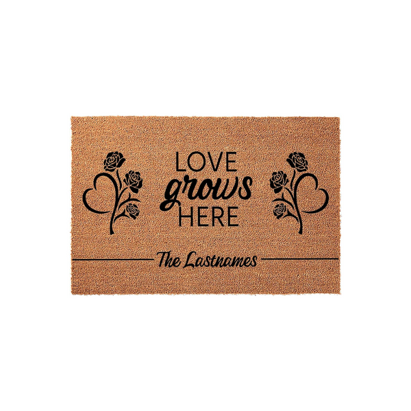 Personalized Love Grows Here coir doormat featuring black printed text and floral heart designs on a natural tan fiber background, providing a welcoming entrance for any family home with space for a custom last name at the bottom.