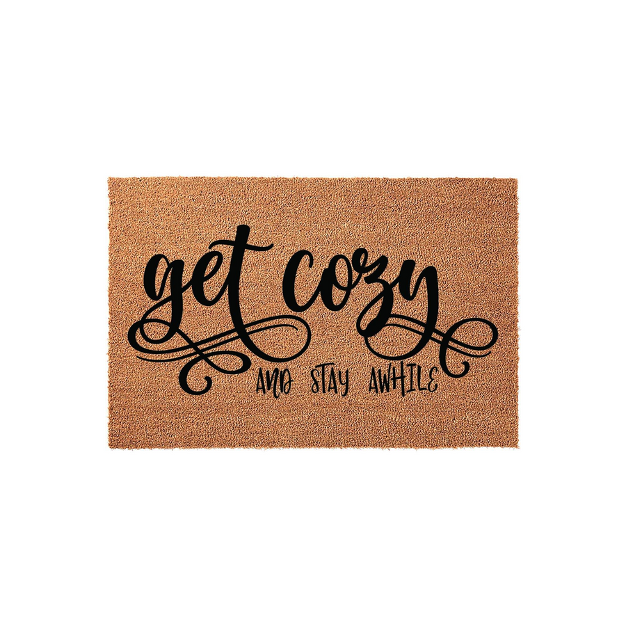 Get Cozy and Stay Awhile coir doormat featuring a natural brown fiber texture and bold black script lettering, designed as a welcoming front porch entrance rug to add a touch of farmhouse charm to your home decor on a plain white
