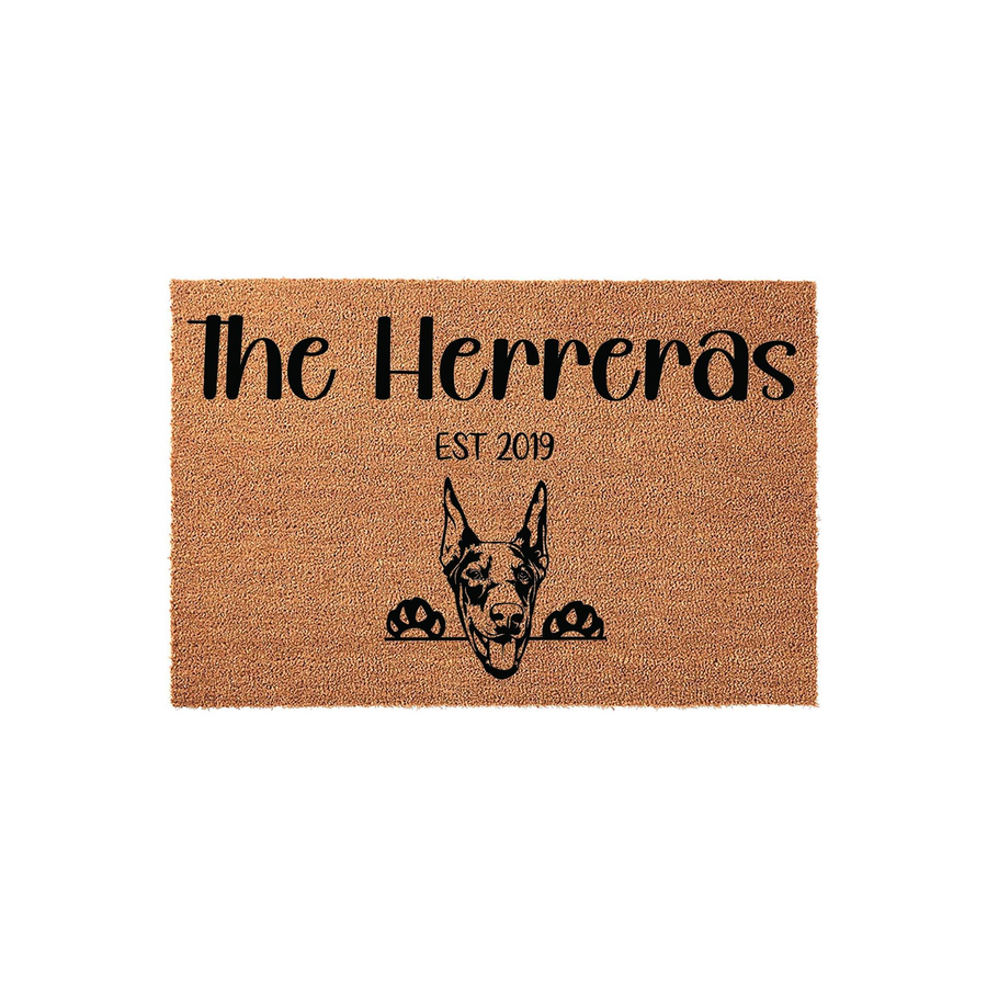 Personalized Doberman Pinscher doormat featuring a natural coir texture with a black printed illustration of a Doberman dog peeking over the bottom edge, customized with a family name and establishment year on a plain white