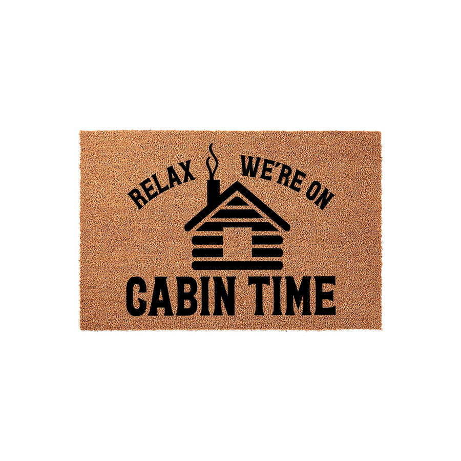 Relax We Are On Cabin Time coir doormat featuring a black graphic of a rustic log cabin with smoke rising from the chimney, set against a natural tan fiber background for a cozy outdoor entrance or a mountain vacation home decor.