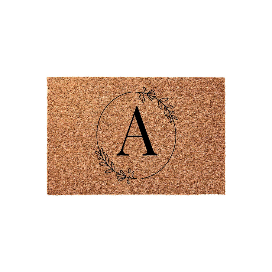 Personalized monogram coir doormat featuring a large black letter A centered inside a delicate hand-drawn floral wreath, set against a natural tan textured background for a classic and welcoming front porch entryway decor style.