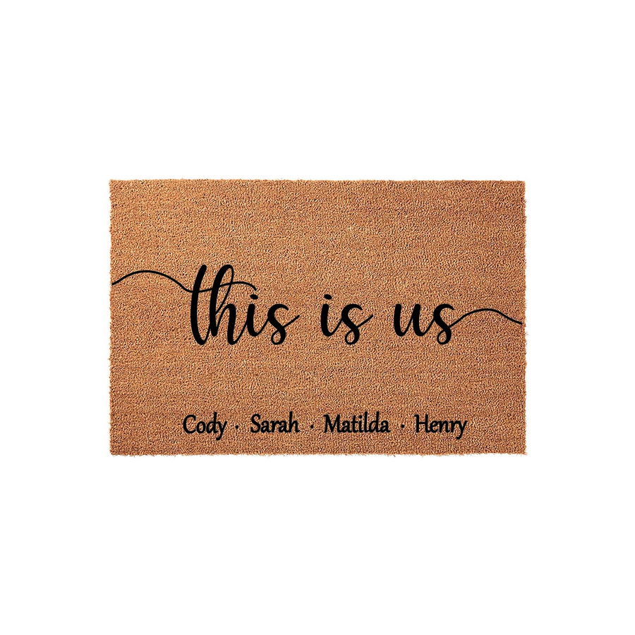 Personalized This Is Us family doormat featuring a natural coir texture with black script lettering and space for custom names, displayed against a clean white background for a modern home entryway or porch decor aesthetic.