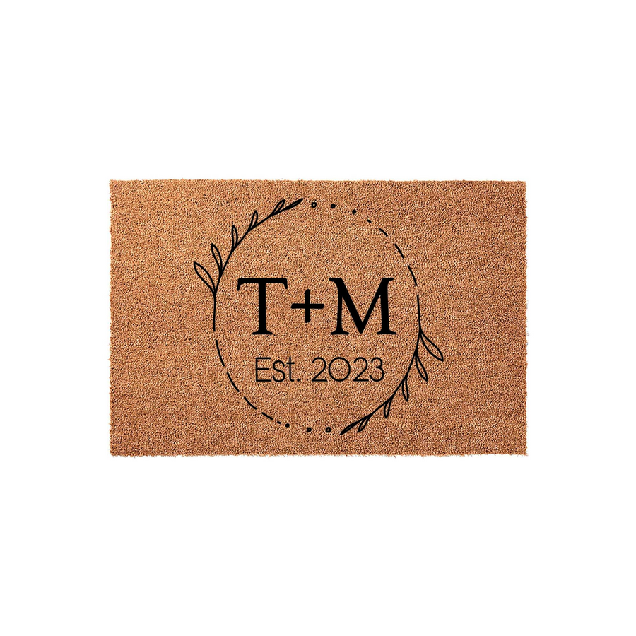 Personalized coir doormat featuring a minimalist black leaf wreath design, centered with custom initials and an established year, providing a durable and welcoming entrance decor piece for a new home or a housewarming celebration.